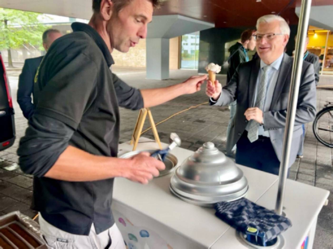Gedeputeerde Gert Harm ten Bolscher krijgt een ijsje van een verkoper bij een ijskar.