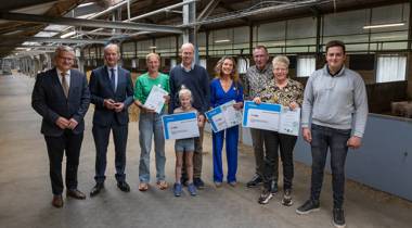 Groep mensen ontvangt prijzen in een agrarische hal, met certificaten en grote cheques.
