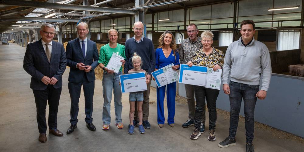 Groep mensen ontvangt prijzen in een agrarische hal, met certificaten en grote cheques.
