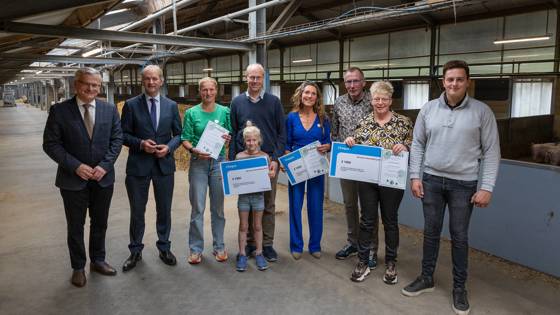 Groep mensen ontvangt prijzen in een agrarische hal, met certificaten en grote cheques.