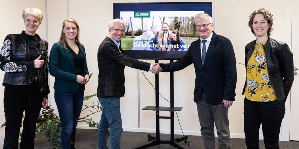 Zes mensen poseren voor een scherm terwijl twee van hen elkaar de hand schudden bij een presentatie over landbouw.