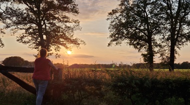 Vrouw kijkt uit over een veld bij zonsondergang.