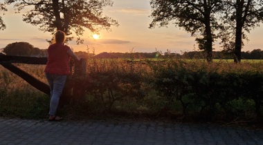 Vrouw kijkt uit over een veld bij zonsondergang.