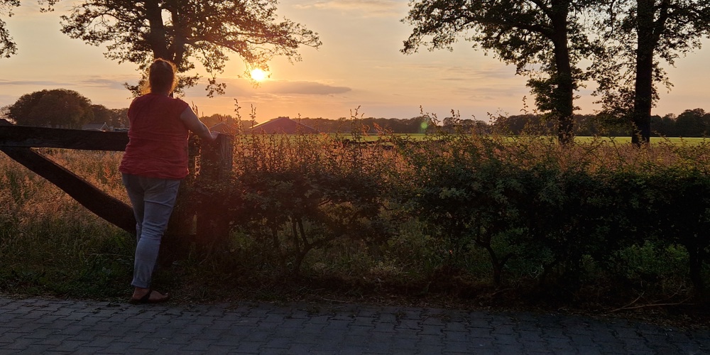 Vrouw kijkt uit over een veld bij zonsondergang.