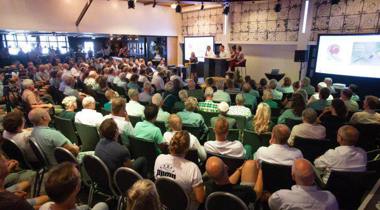 Een groep mensen woont een bijeenkomst bij in een grote zaal.