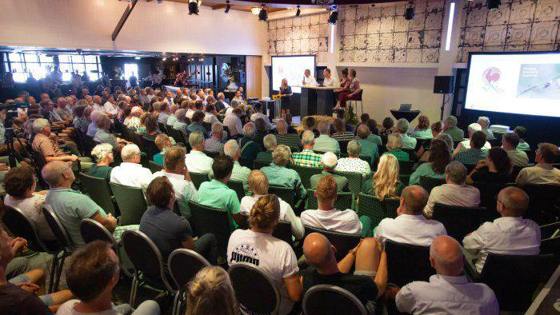 Een groep mensen woont een bijeenkomst bij in een grote zaal.