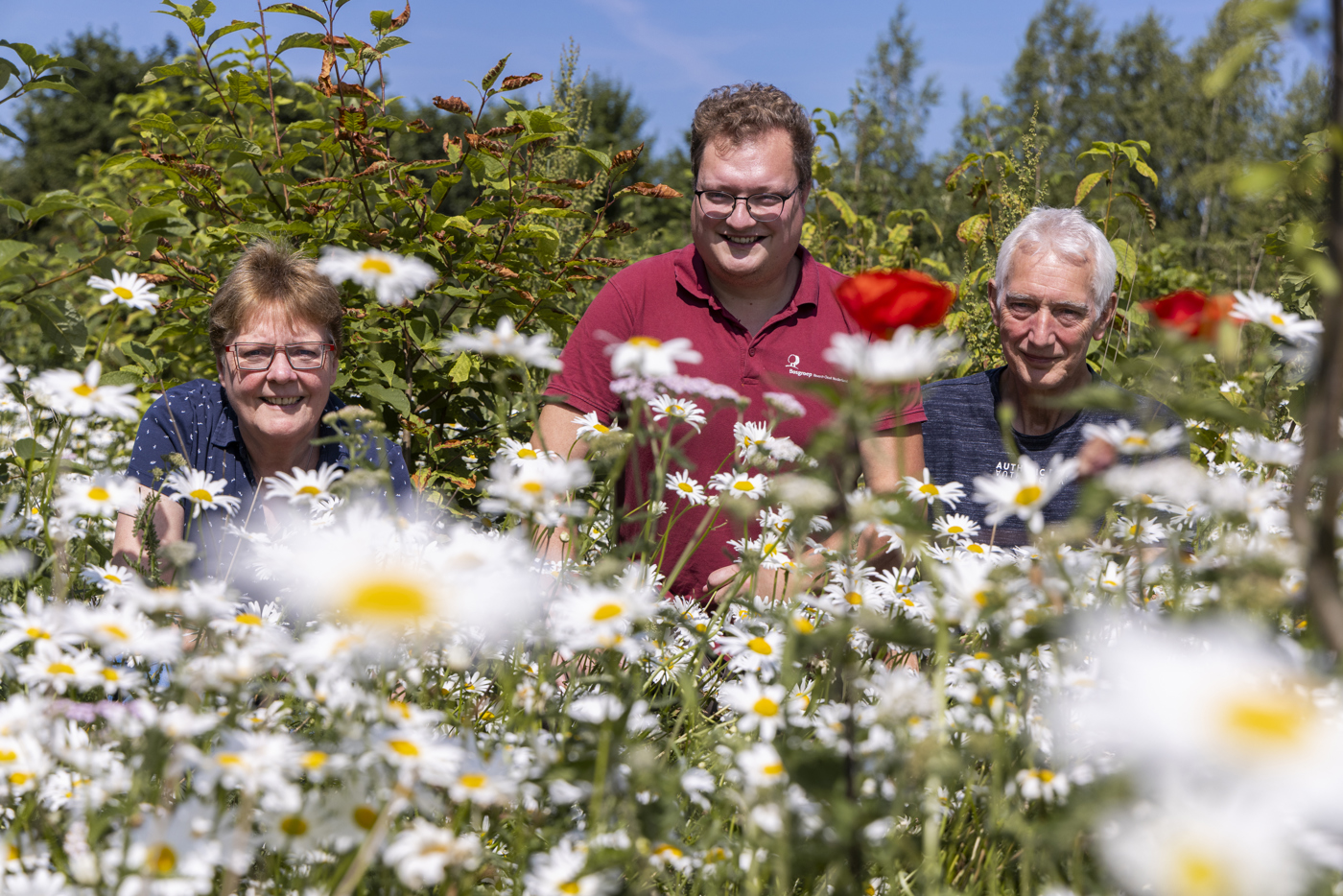 3 personen poseren tussen bloemen en struiken
