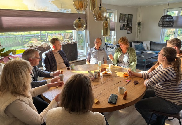 Gesprek rond de eetkamertafel tijdens een van de bezoeken met 8 mensen rond de tafel, waaronder de gedeputeerde.