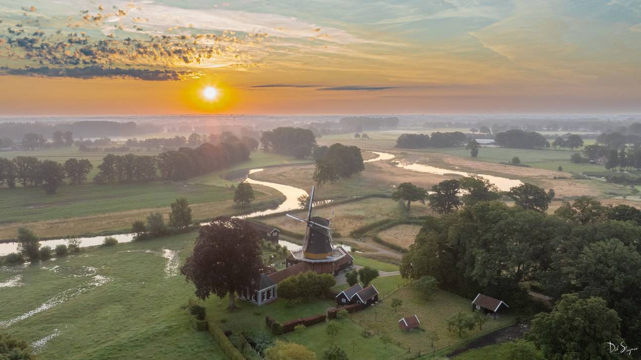 Windmolen bij zonsopgang in een groen landschap met rivier.