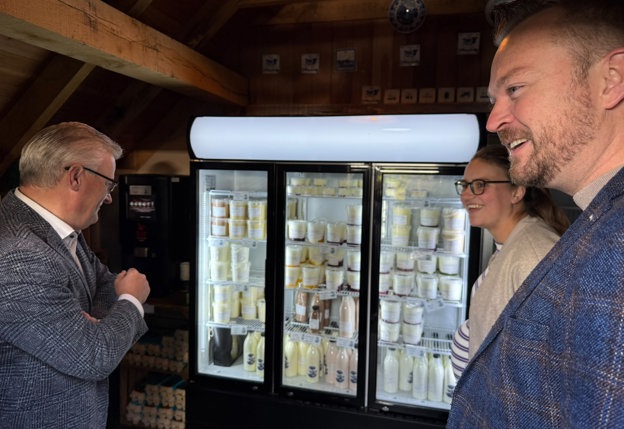 De gedeputeerde (links) bekijkt een deel van de collectie van de IJsboerderij in een brede koeling met 3 glazen deuren met daarachter verschillende producten.