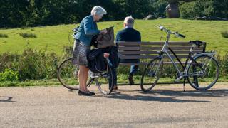 Twee fietsers nemen pauze op een bankje bij een hunebed, met fietsen en wegwijzerbord in beeld.