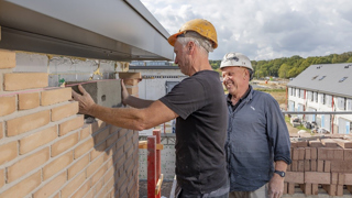 Twee mensen met witte werkhelmen zetten grijze baksteen tussen muur