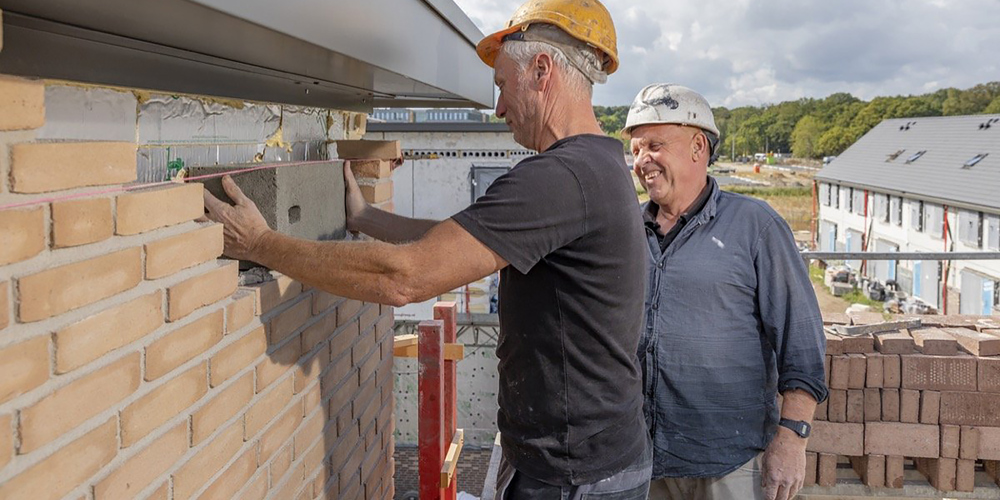 Twee mensen met witte werkhelmen zetten grijze baksteen tussen muur