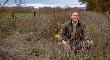 Man zit in een veld met hoge, droge planten in een herfstlandschap.