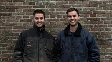 Laurens en Rutger Pelgrom poseren al lachend. Ze staan voor een bakstenen muur.