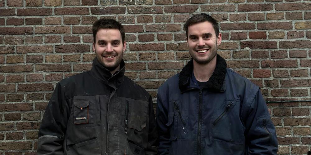 Laurens en Rutger Pelgrom poseren al lachend. Ze staan voor een bakstenen muur.